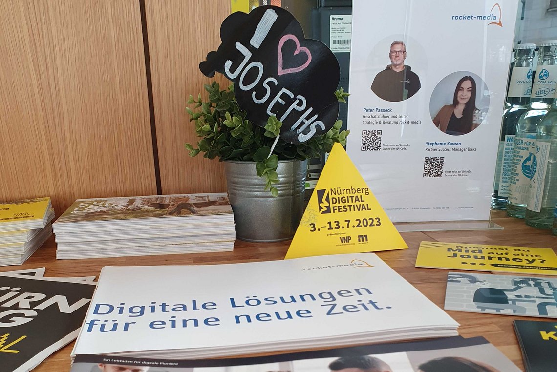 Aufnahme von Broschüren auf einem Tisch, im Hintergrund die gelben Aufsteller des Nürnberg Digital Festivals.