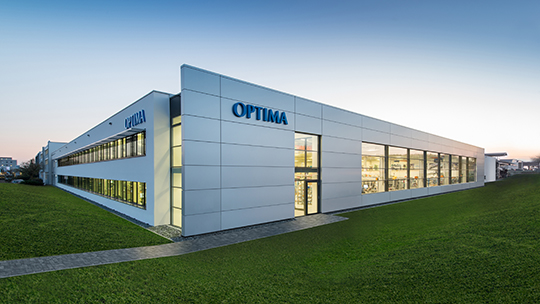 Unternehmensbild von Optima, ein Industriegebäude von außen auf einer grünen Wiese.